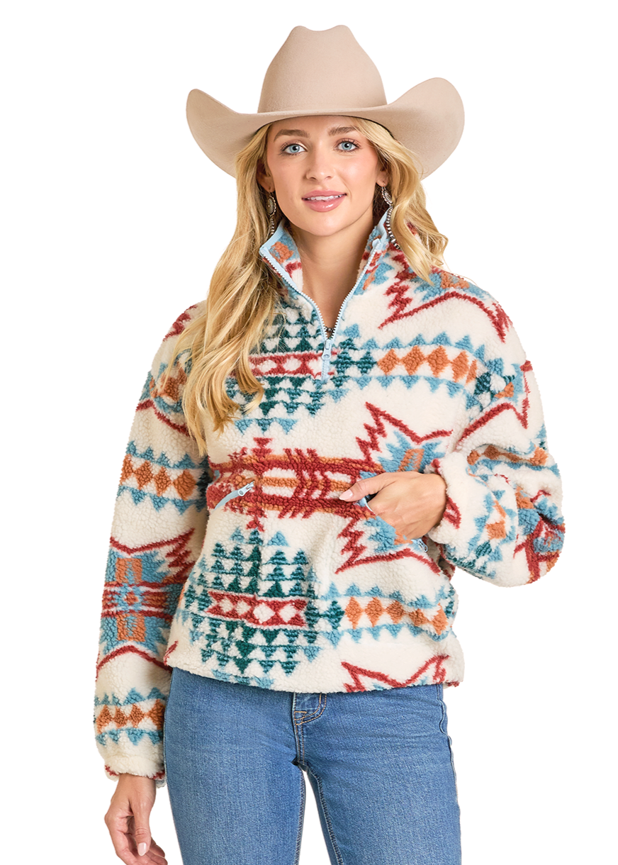 A woman with long blonde hair wears the Rock & Roll Denim Aztec Sherpa Pullover, featuring a southwestern design, along with a tan cowboy hat and blue jeans, standing against a plain light background and looking at the camera.