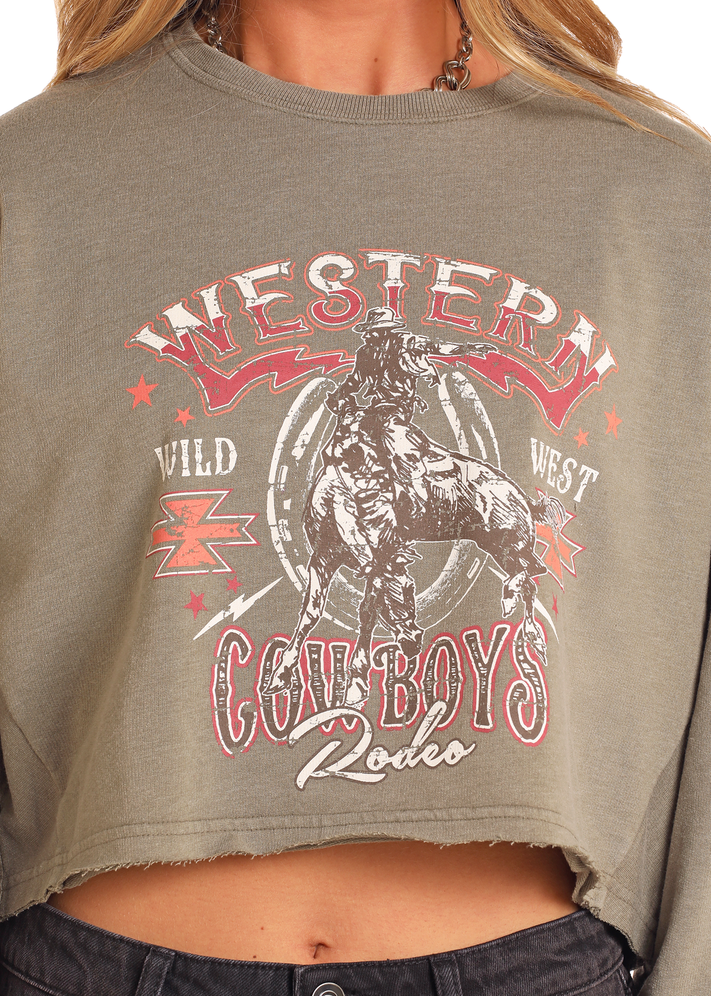 A close-up shows a person wearing the Rock & Roll Denim Western Graphic Pullover in olive green, featuring a bold cowboy and horse graphic with "Western Cowboys Rodeo" and "Wild West" text, plus star and lightning bolt accents.