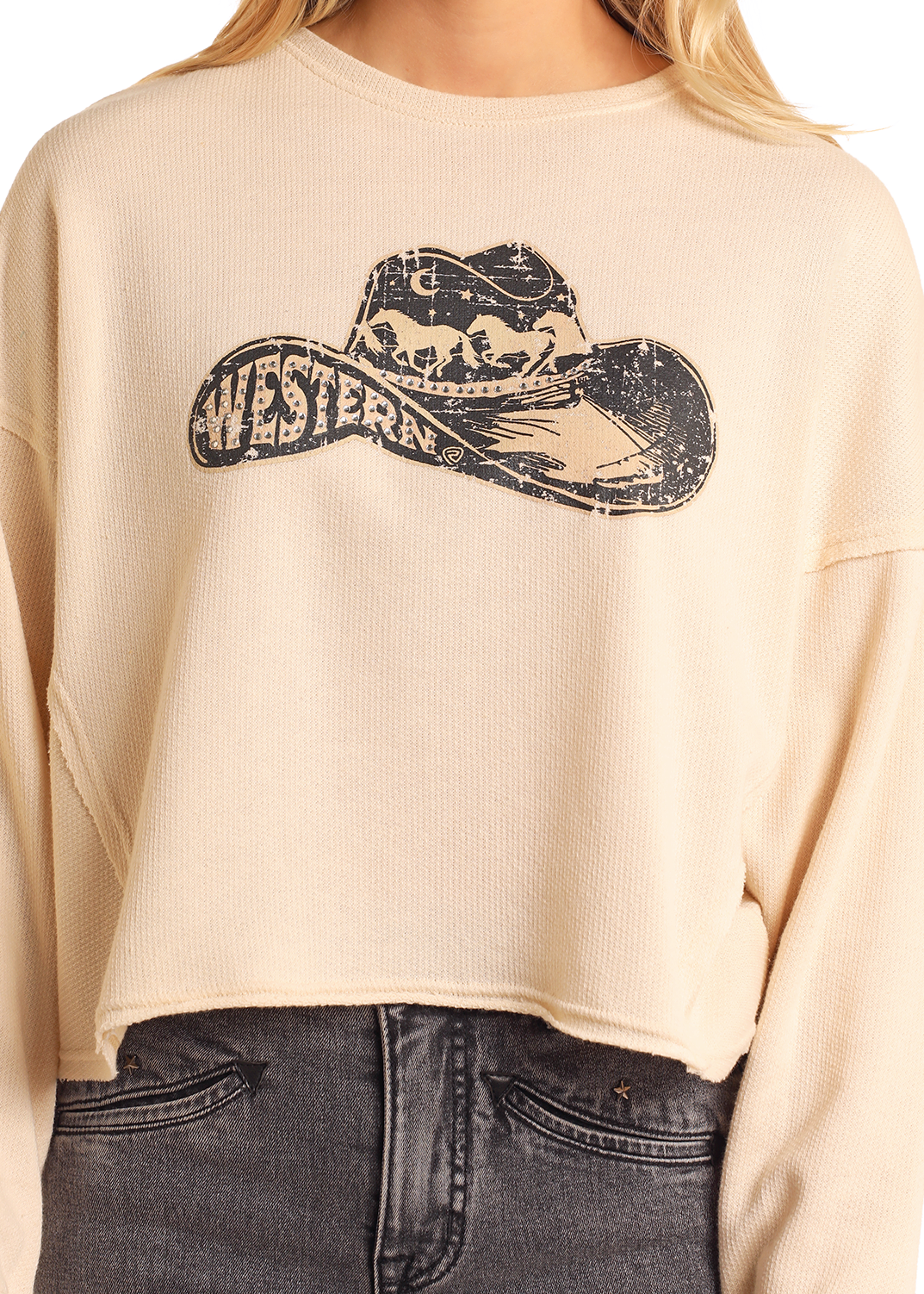 Someone wears the Rock & Roll Denim Western Cropped Pullover—a beige waffle knit long-sleeve top with a cowboy hat horse graphic and "WESTERN" text—paired with high-waisted black jeans.