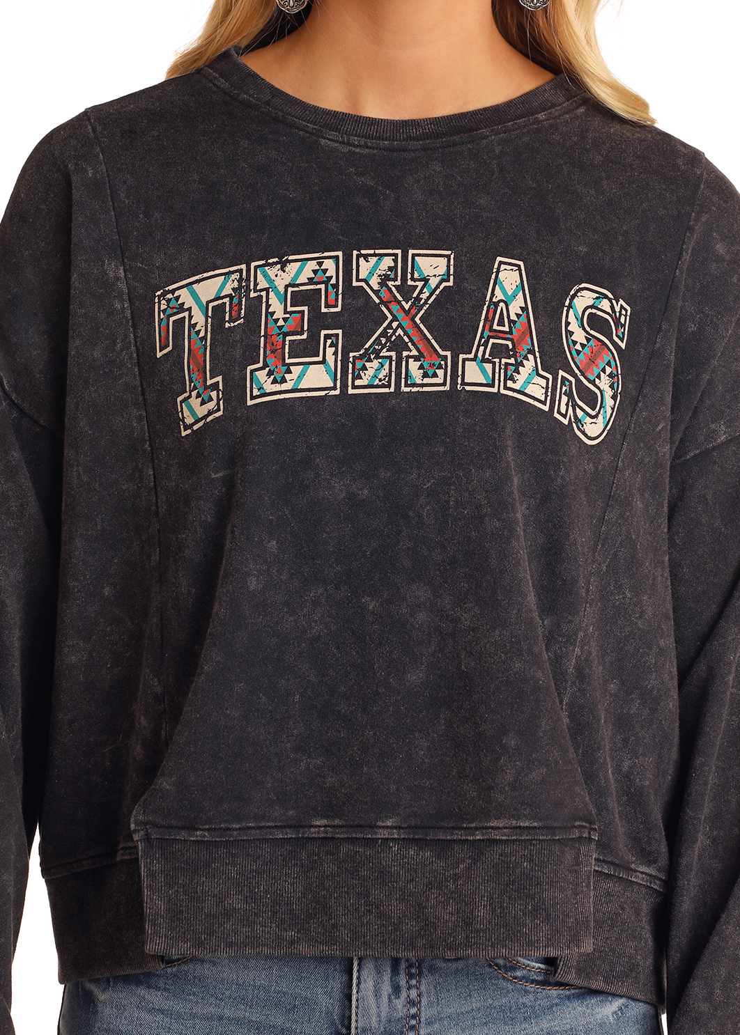 A person wears the Rock & Roll Denim Texas Graphic Pullover, featuring bold, patterned TEXAS lettering across the chest in black acid-wash. Only the torso of this standout sweatshirt is shown.