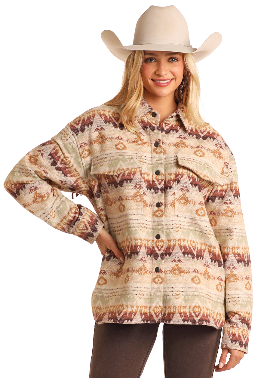 A woman in a beige cowboy hat and Rock & Roll Denim’s Fringe Aztec Shacket—a 100% cotton shirt jacket with southwestern designs—stands smiling, hand on hip, against a plain background; it’s perfect for casual outfits.