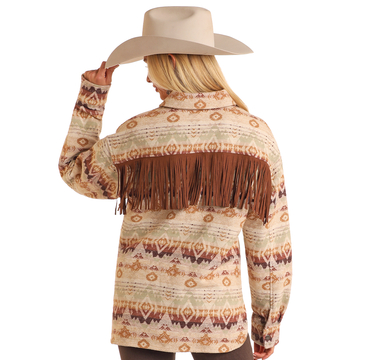 A woman in the Rock & Roll Denim Fringe Aztec Shacket, a 100% cotton Western-style shirt jacket with brown fringe, and a wide-brimmed beige cowboy hat faces away holding her hat—a timeless casual look.