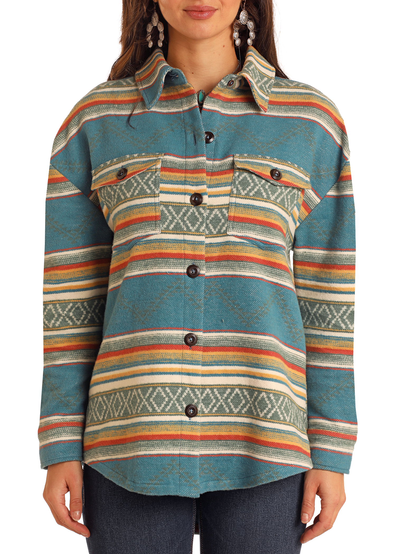 A woman layers the Rock & Roll Denim Turquoise Aztec Shacket—featuring horizontal multicolored stripes, geometric patterns, chest pockets, and dark buttons—with dark jeans for a casual look.