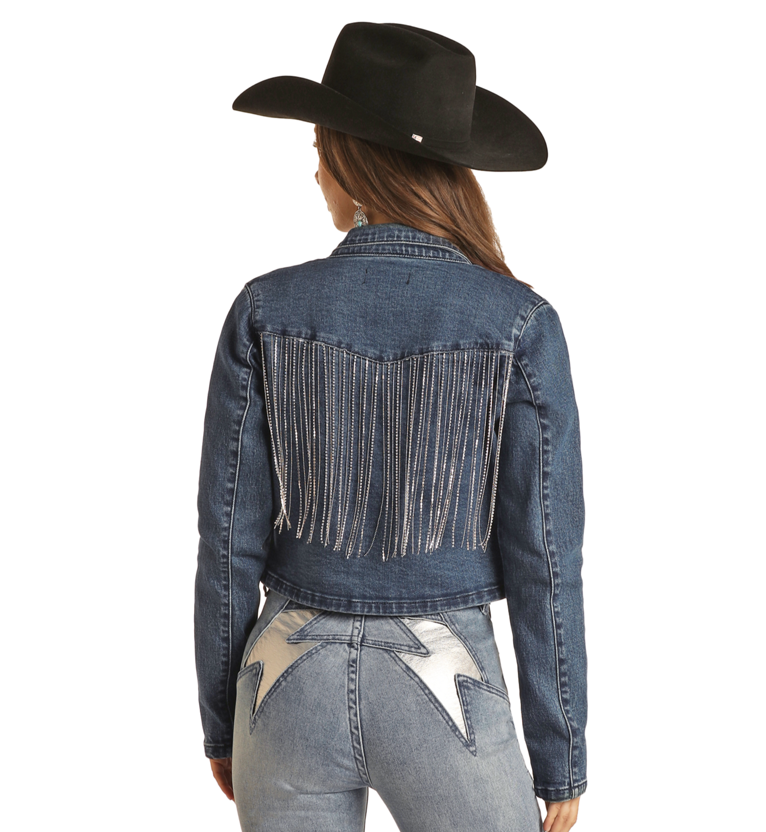 A woman faces away from the camera wearing a black cowboy hat and the Rock & Roll Denim Rhinestone Fringe Cropped Denim Jacket, paired with light blue jeans with large silver stars on the pockets.