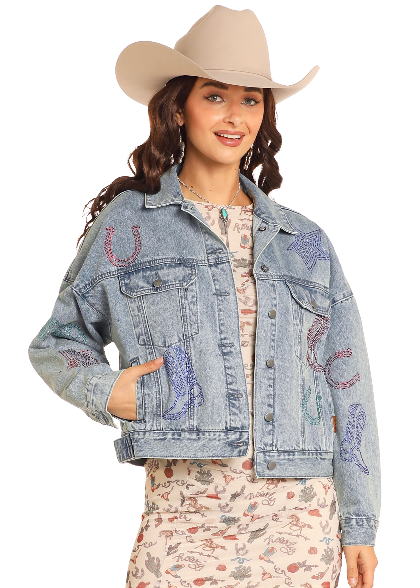 A woman smiles with one hand in her pocket, wearing the Rock & Roll Denim Studded Western Denim Jacket, a light cowboy hat, and a printed dress.