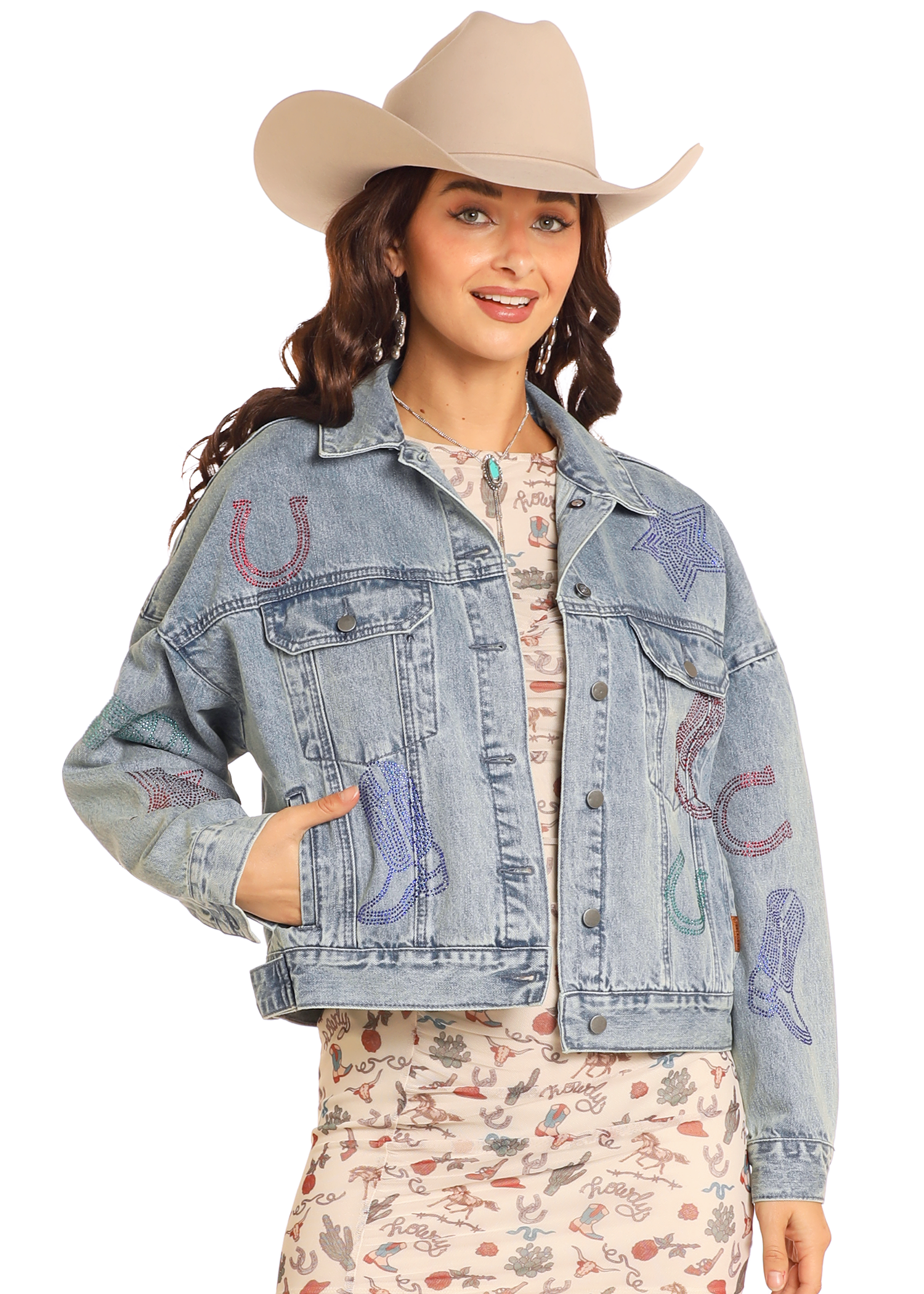 A woman smiles with one hand in her pocket, wearing the Rock & Roll Denim Studded Western Denim Jacket, a light cowboy hat, and a printed dress.