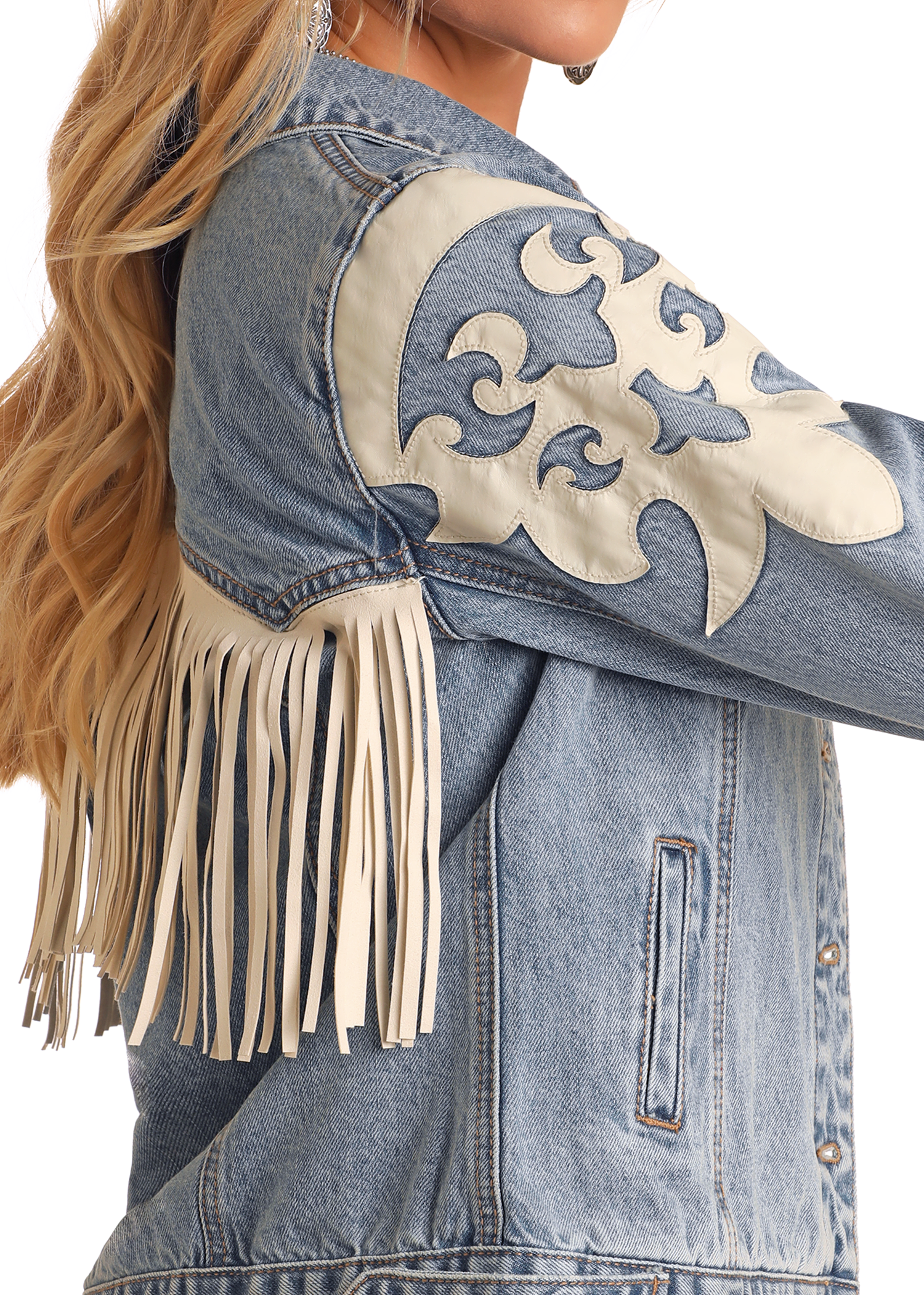 A woman with long blonde hair wears the Rock & Roll Denim Pleather Fringe Denim Jacket—a blue denim piece with tan pleather fringe and white appliqué designs on the shoulder and sleeve.