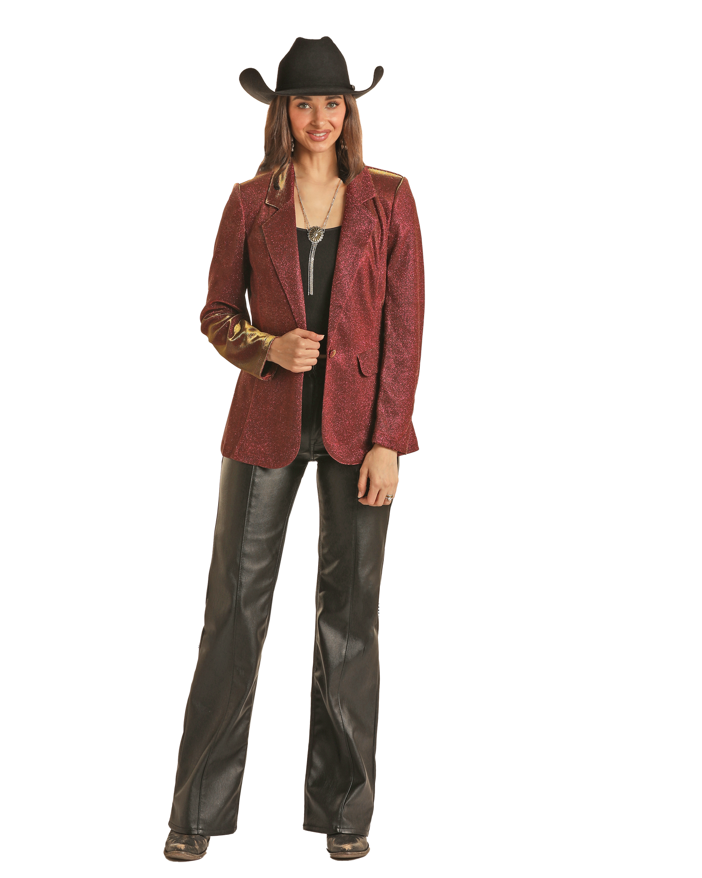 A woman in a Rock & Roll Denim Red Iridescent Blazer, black cowboy hat, black top, black leather pants, and boots stands smiling against a plain white background.