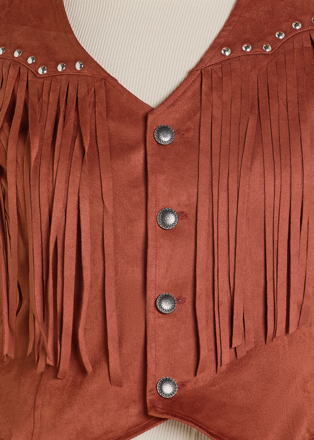 Close-up of the Rock & Roll Denim Studded Fringe Microsuede Vest featuring silver buttons, long fringe, and stud detailing, styled over a cream ribbed shirt.