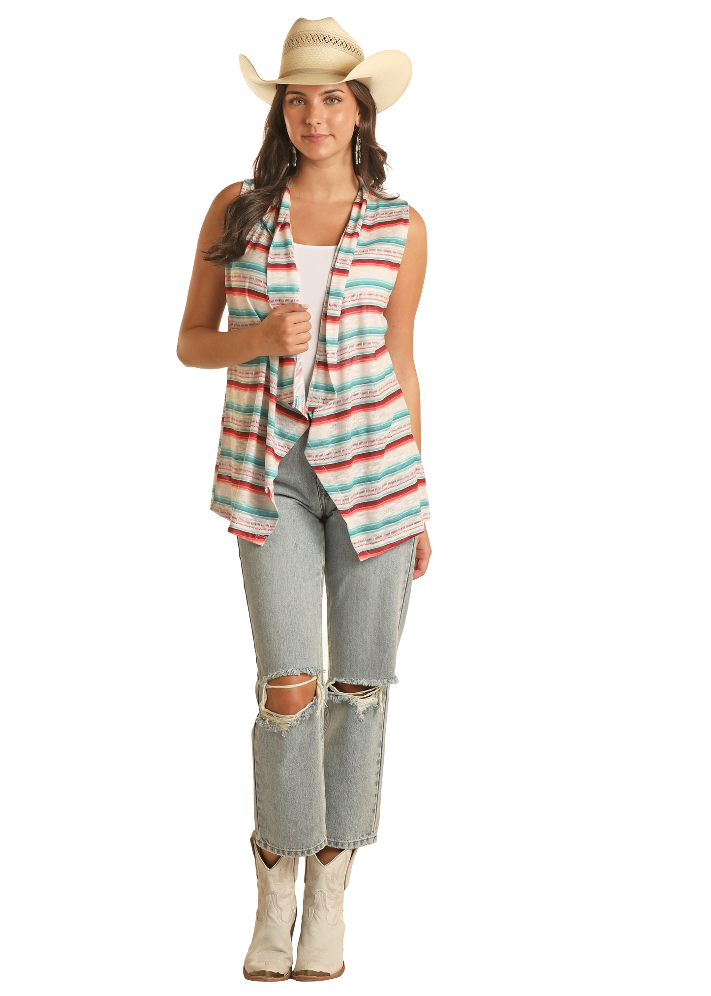 A woman stands facing forward against a plain background, wearing a Rock & Roll Denim Serape Vest over a white top, ripped jeans, white cowboy boots, and a cowboy hat.