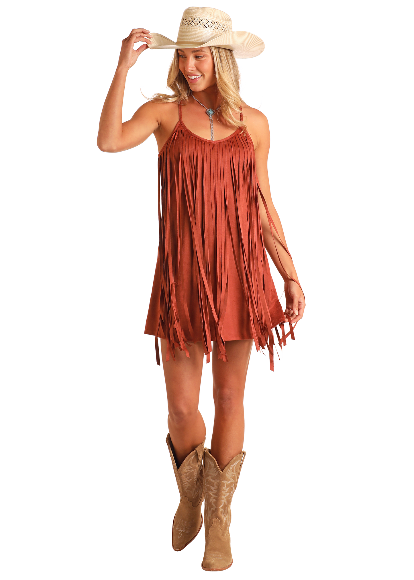 A woman wearing the Rock & Roll Denim Microsuede Fringe Dress and tan cowboy boots smiles as she holds her hat and walks forward.