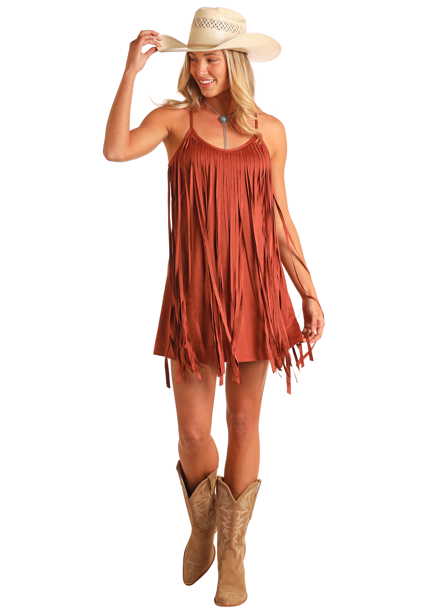 A woman wearing the Rock & Roll Denim Microsuede Fringe Dress and tan cowboy boots smiles as she holds her hat and walks forward.