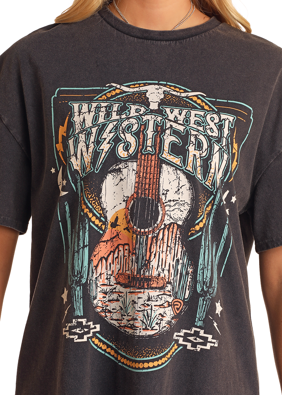 A person wears the Rock & Roll Denim Wild West Western T-Shirt Dress - M, a black dress with a colorful skull, guitar, and cacti graphic and "WILD WEST WESTERN" printed across the chest.