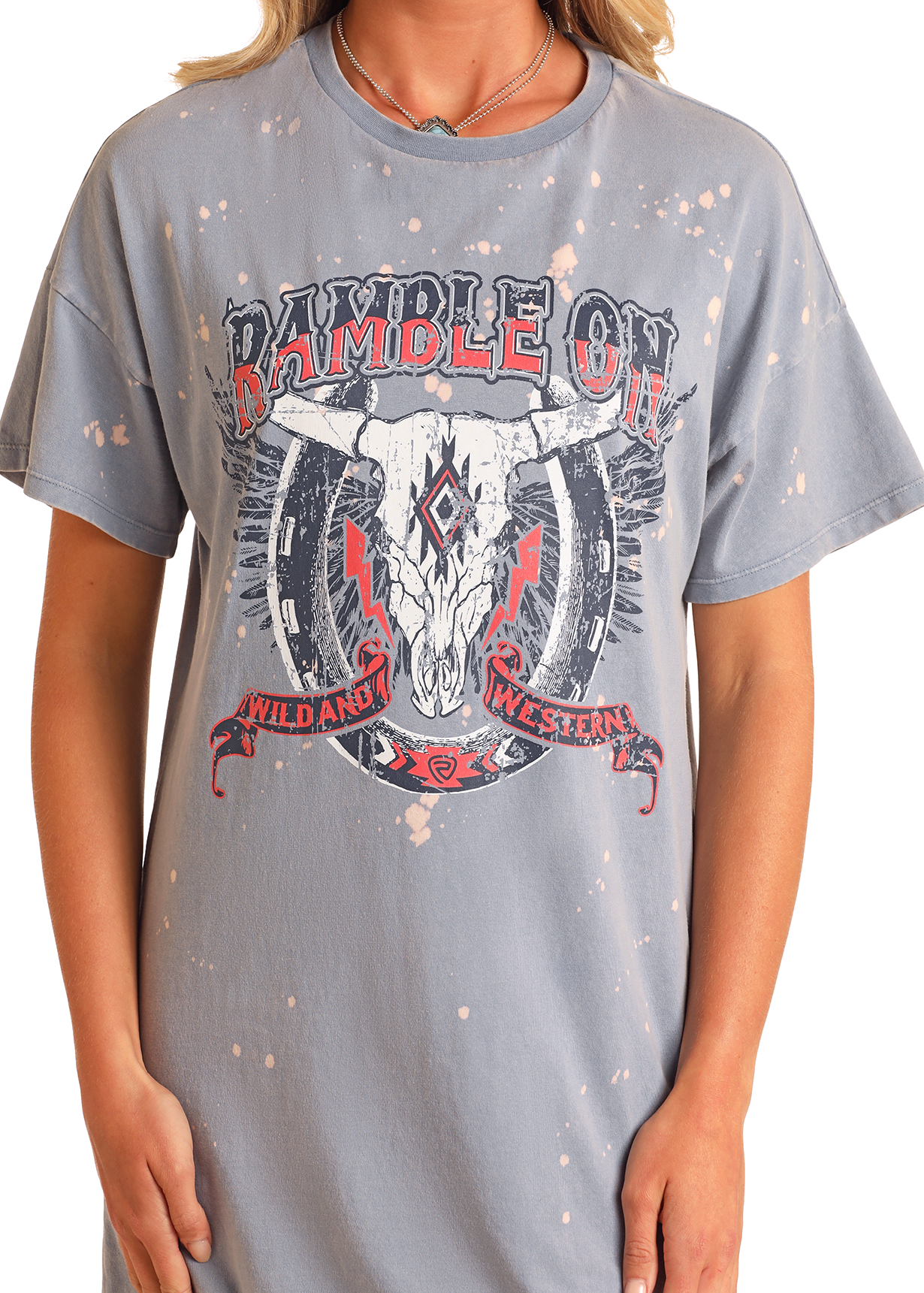 A person wears the Ramble On T-Shirt Dress by Rock & Roll Denim—a light gray, oversized style with a distressed finish. The casual dress features a steer skull graphic and geometric patterns with text: RAMBLE ON and WILD AND WESTERN.
