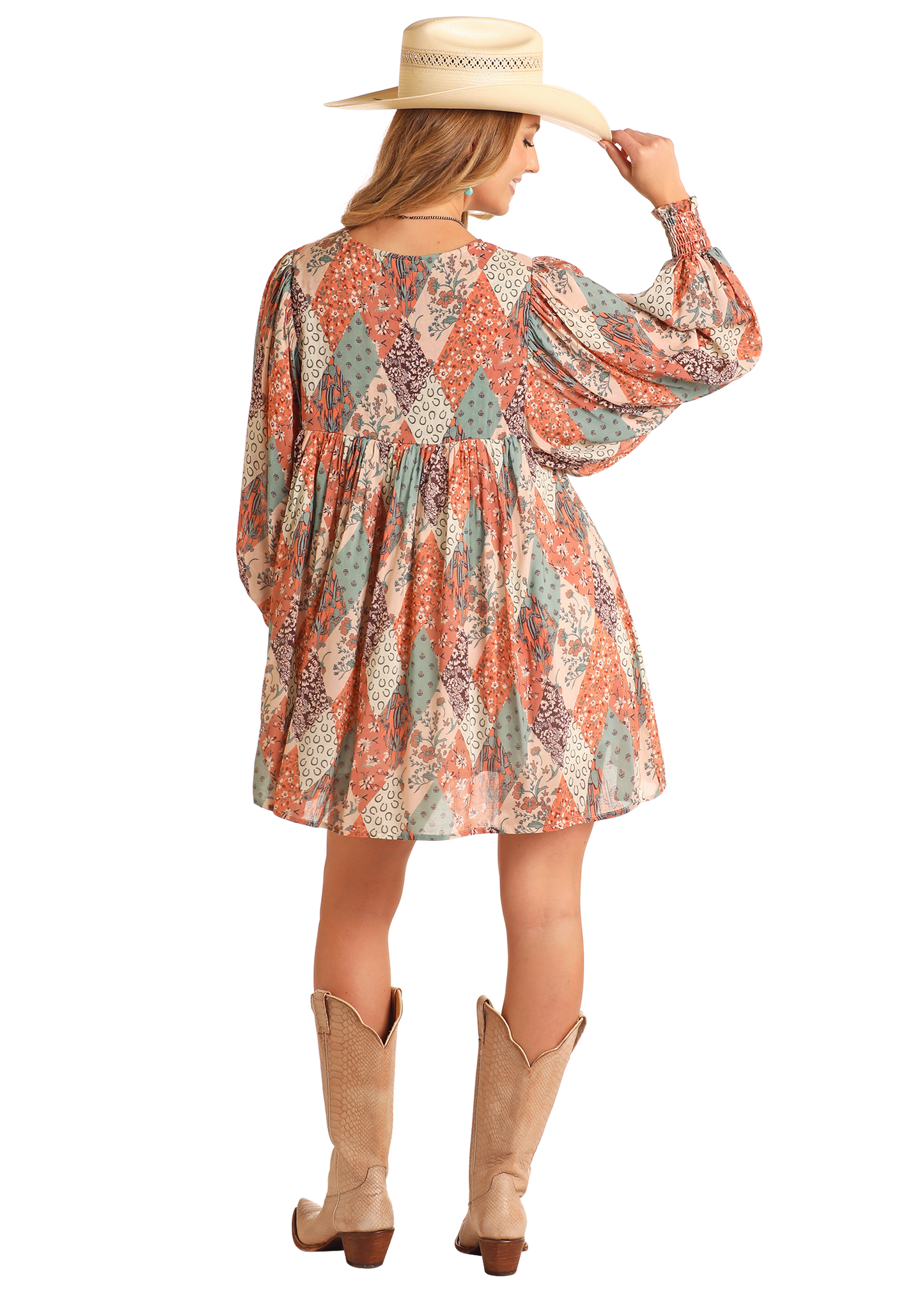 A woman in the Rock & Roll Denim Patchwork Print Mini Dress, wide-brimmed hat, and tan cowboy boots stands facing away, holding her hat’s brim—an effortlessly stylish everyday look.