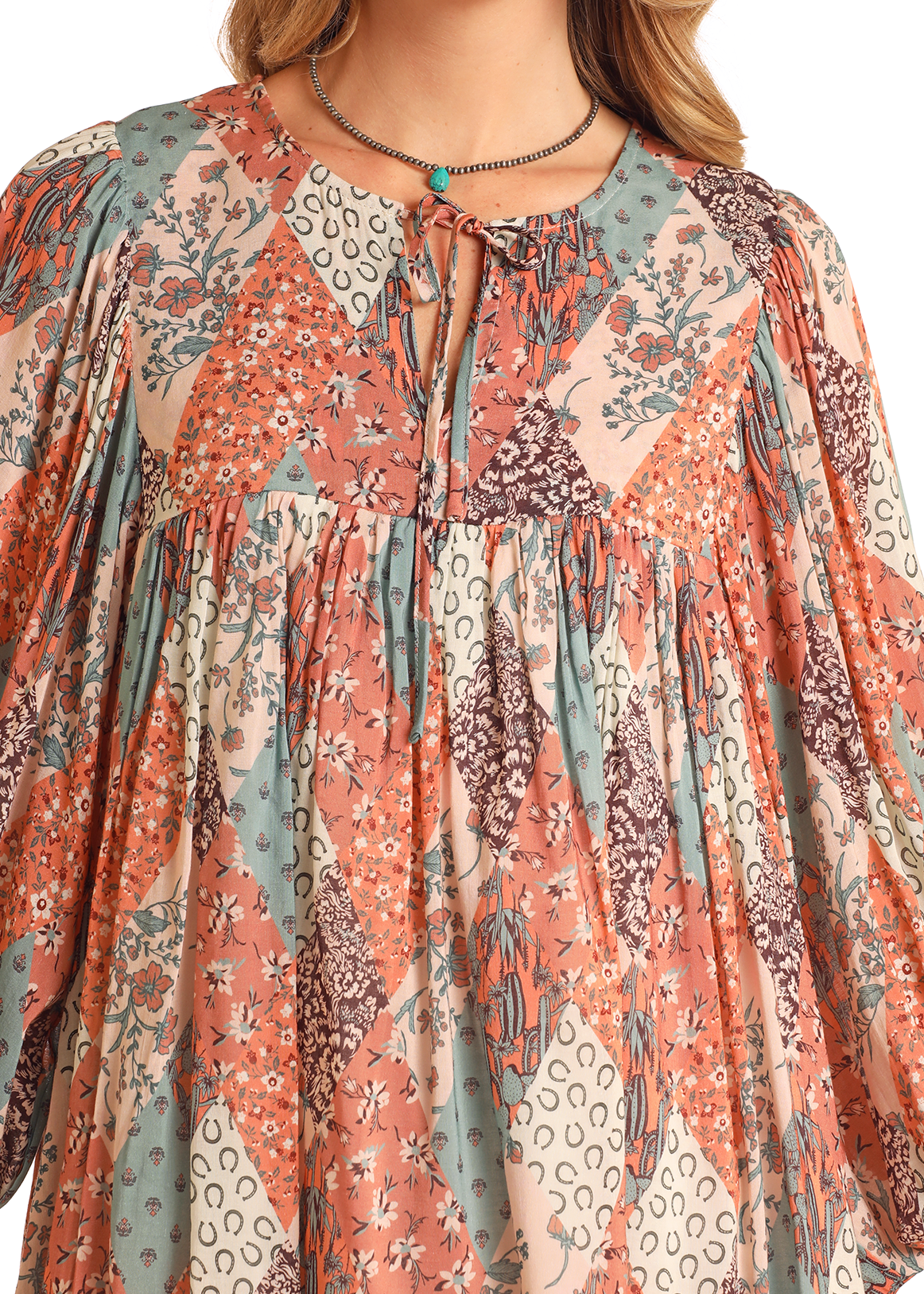A close-up of a woman wearing the Rock & Roll Denim Patchwork Print Mini Dress with colorful floral and animal patterns, round neckline with keyhole tie, long sleeves, and a beaded necklace—ideal for everyday style.