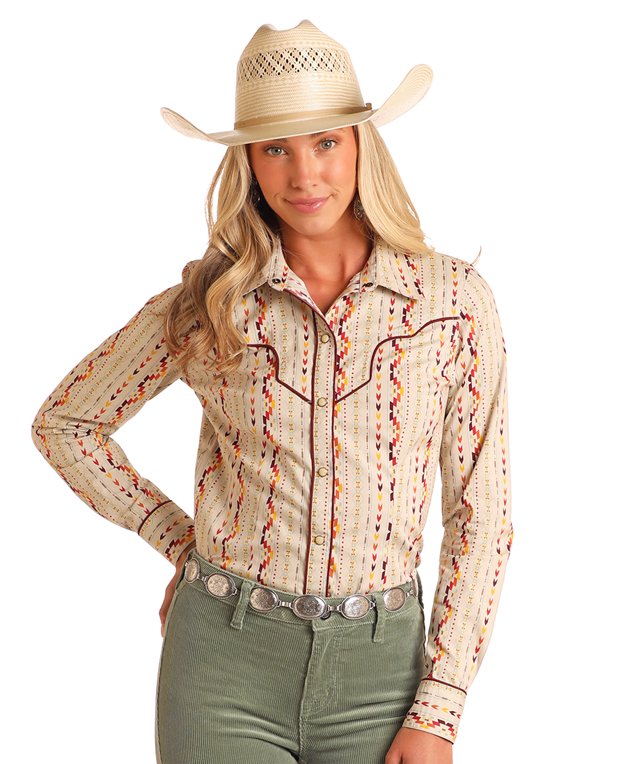 A woman in a cream cowboy hat and green corduroy pants poses confidently against a white background, wearing the Rock & Roll Denim Aztec Striped Long Sleeve Snap Shirt and a silver concho belt.