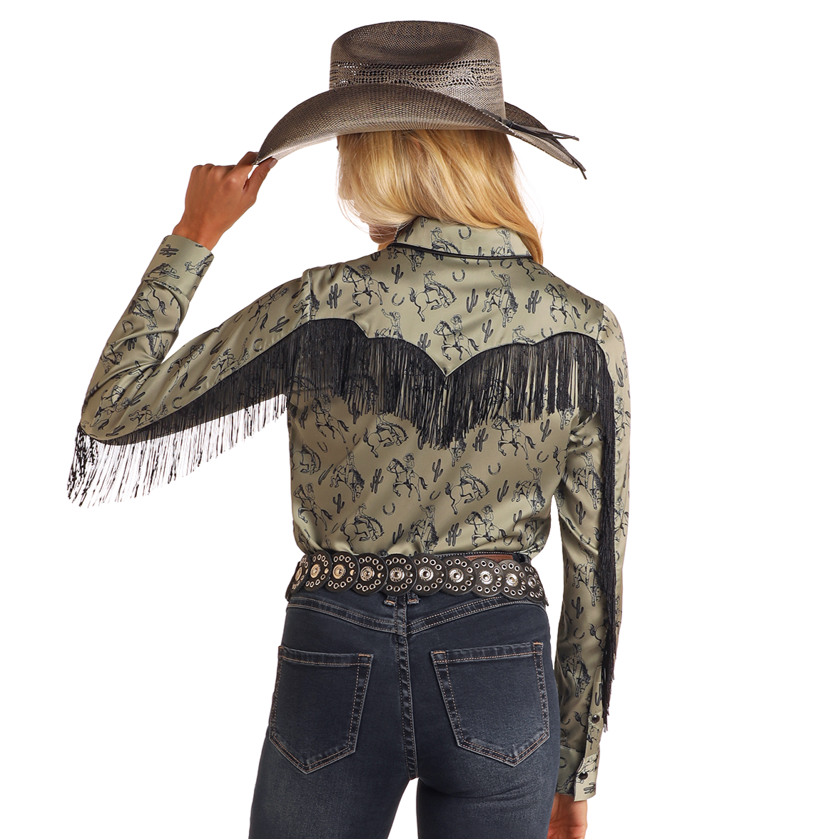 A woman in a cowboy hat faces away, wearing the Rock & Roll Denim Western Print Long Sleeve Satin Shirt with black fringe and designs, paired with dark denim jeans and a decorative belt.