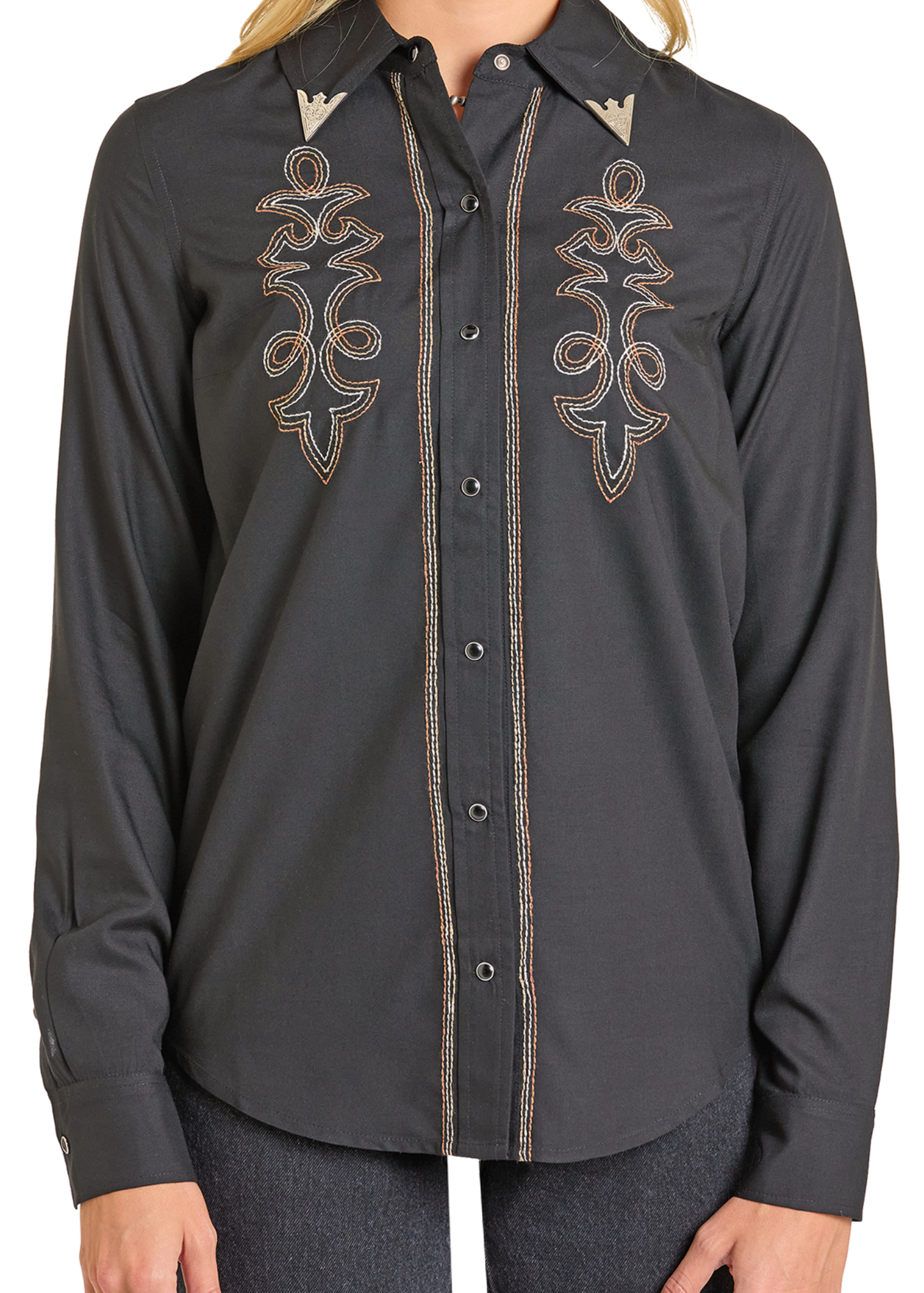 A person wears the Rock & Roll Denim West Desperado Boot Stitch Snap Shirt—a fitted black top with detailed beige embroidery on the chest and collar, long sleeves, and a modern western vibe. Only their upper body is visible.