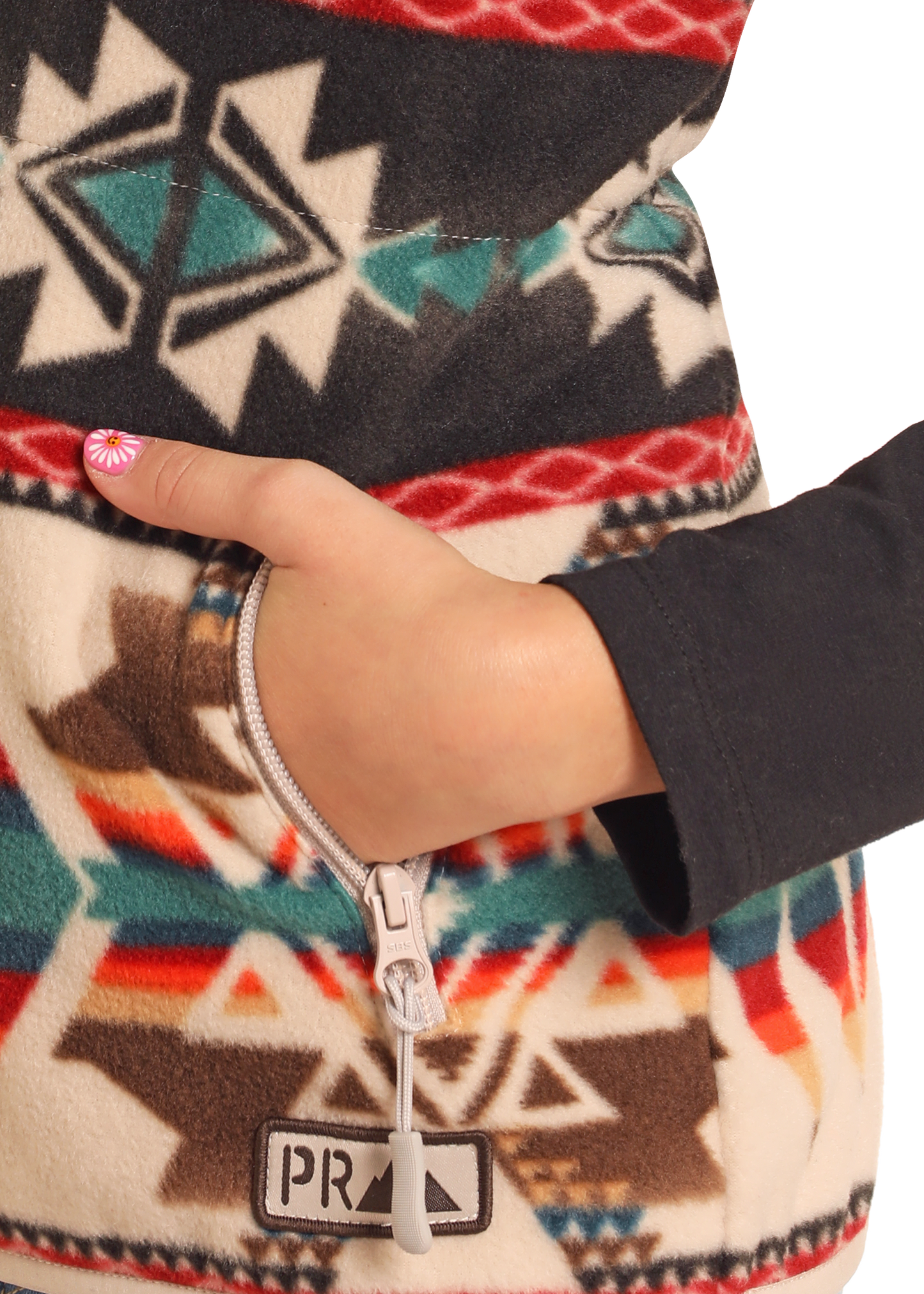 A hand with painted nails is partly tucked into a zippered pocket of the Rock & Roll Denim Kids' Cream Aztec Fleece Vest, showcasing its colorful geometric pattern and visible PRA label.