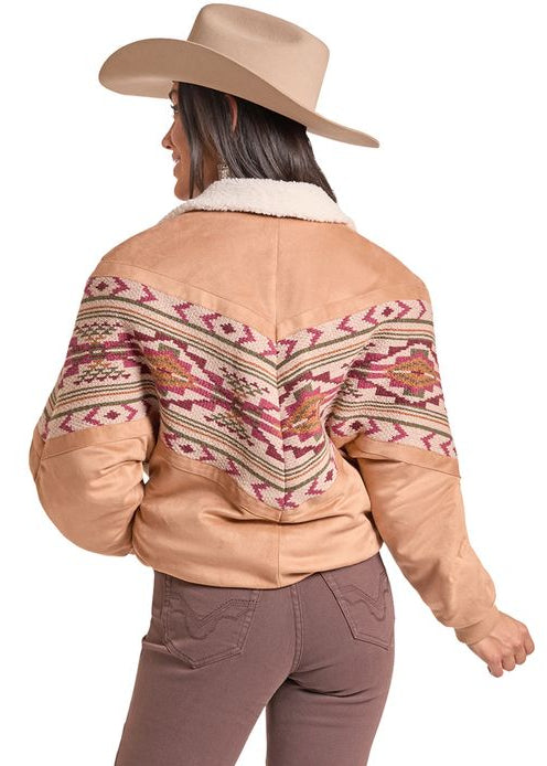 A woman shown from the back wearing a tan western-style jacket with a colorful geometric pattern on the back, brown flared pants, and a tan cowboy hat, set against a plain white background.