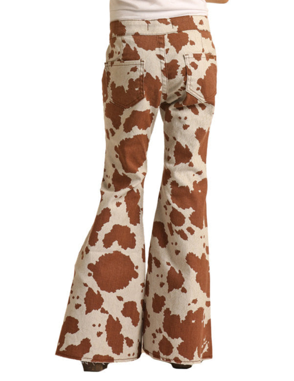 A little cowgirl is seen from behind in Rock & Roll Denim Girls' Cow Print Bell Bottom Jeans, featuring a high waist, large back pockets, flared legs, and a bold brown and white pattern with a white top.