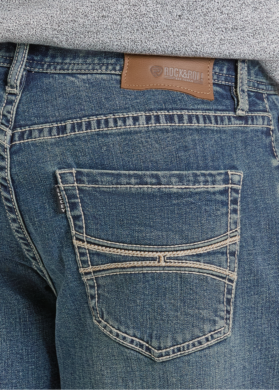 Close-up of the back of a person wearing blue Hooey Relaxed Fit Raised Embroidery Pocket Stackable Bootcut Jeans by Rock & Roll Denim, featuring a brown leather patch on the waistband and a grey sweater tucked in above the jeans.
