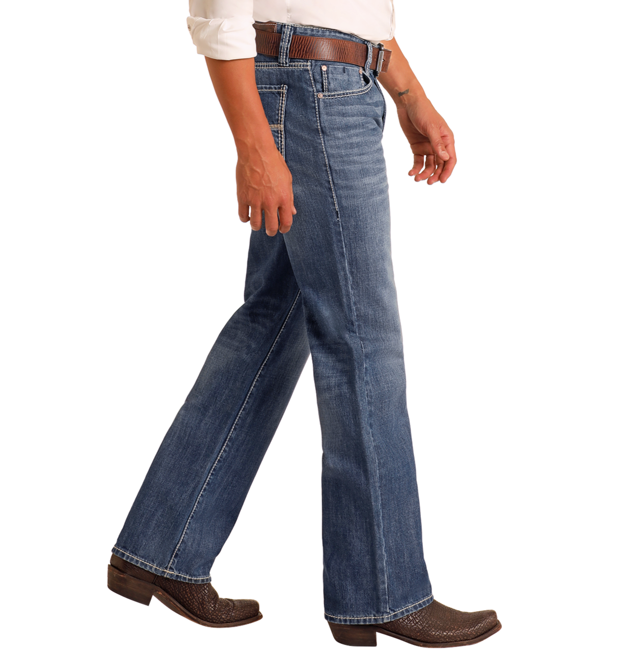 A person wears Rock & Roll Denim Relaxed Fit Medium Wash Straight Leg Jeans with a brown belt and cowboy boots, paired with a white rolled-sleeve shirt. Only the lower body and part of one arm are visible against a plain white background.