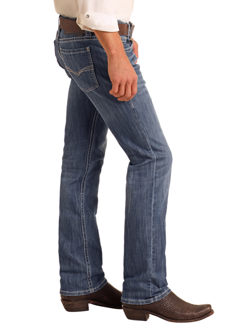 A person in Rock & Roll Denim Slim Fit Straight Leg Jeans, a white shirt, brown belt, and brown cowboy boots stands sideways against a plain light background.