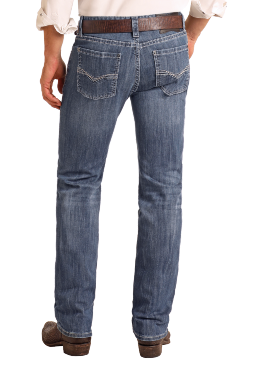 A man wearing Rock & Roll Denim Slim Fit Straight Leg Jeans, a brown belt, brown shoes, and a white shirt stands with his back to the camera against a plain light background.