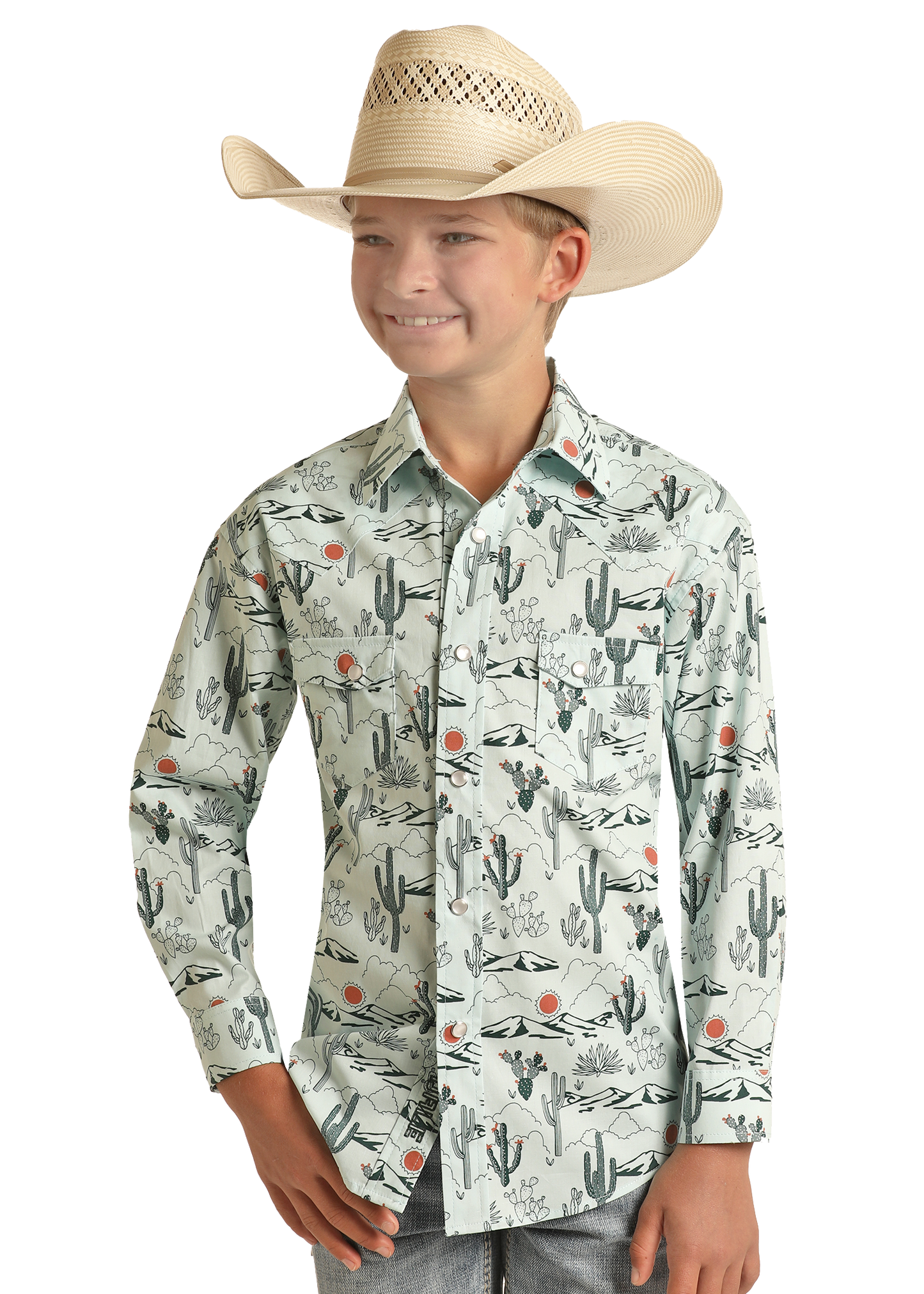 A boy wearing a straw cowboy hat and a Rock & Roll Denim Boys' Dale Brisby Cactus Print Long Sleeve Snap Shirt smiles with one hand in his pocket against a plain background.