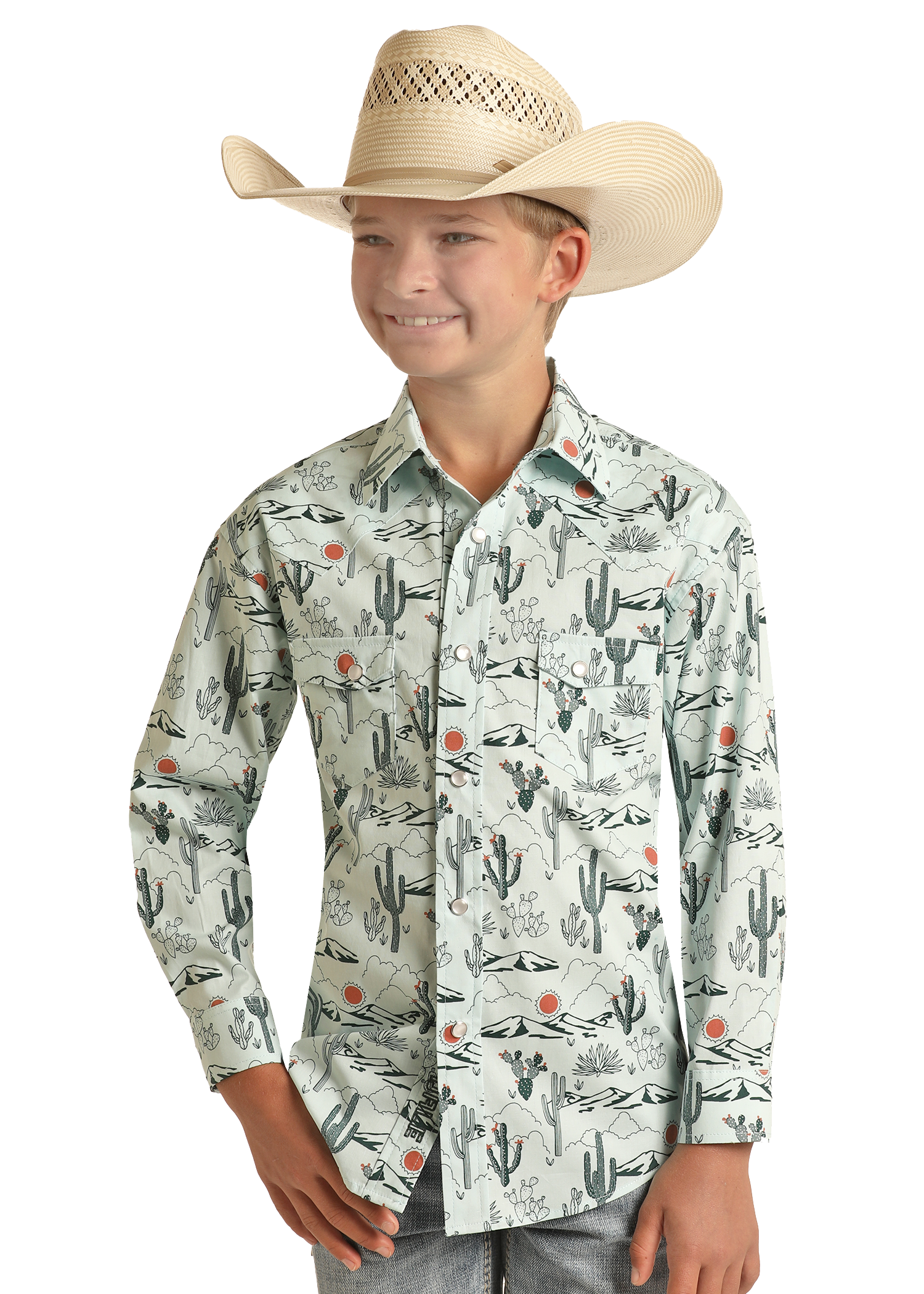 A boy wearing a straw cowboy hat and a Rock & Roll Denim Boys' Dale Brisby Cactus Print Long Sleeve Snap Shirt smiles with one hand in his pocket against a plain background.