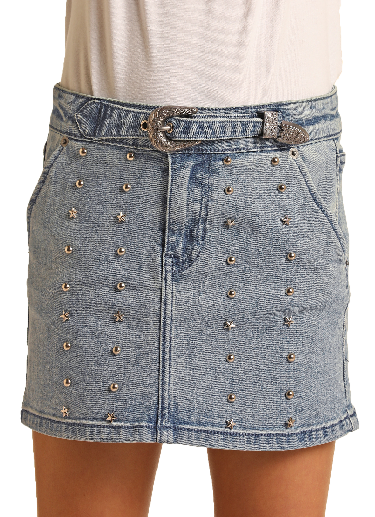 A girl wears the Rock & Roll Denim Girls' Studded Denim Skirt with a high-rise waist, silver studs, star-shaped embellishments, a decorative silver buckle belt, two front pockets, and pairs it with a white top for a western-inspired look.