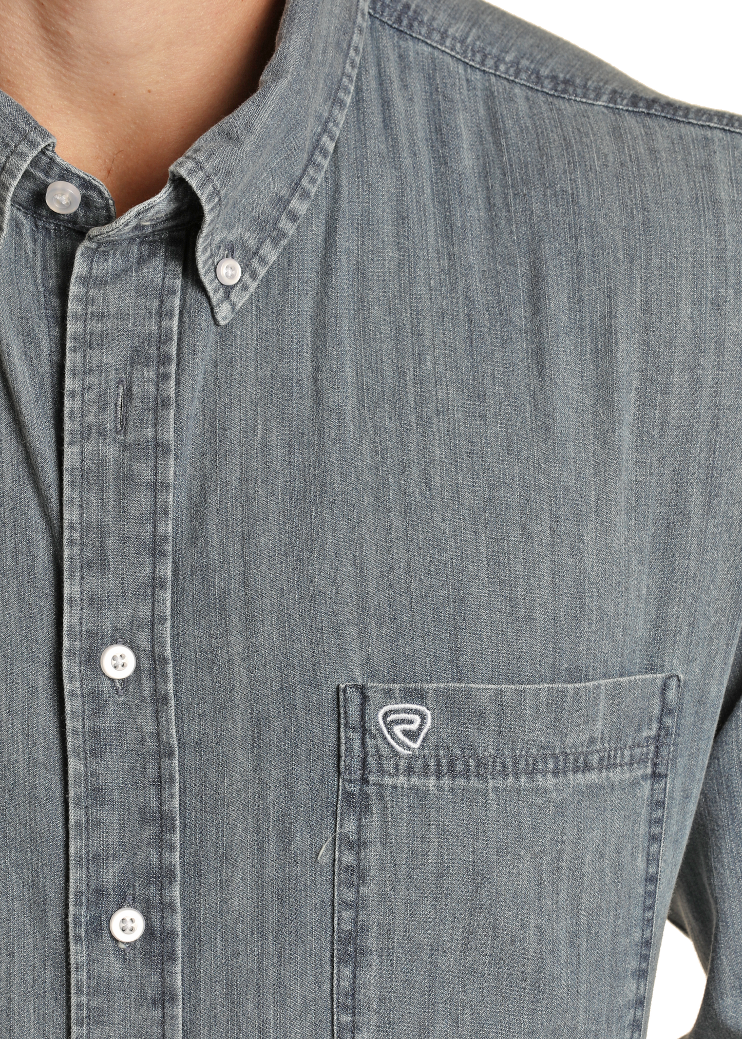 A close-up of a person wearing the Rock & Roll Denim Long Sleeve Button Shirt, featuring a chest pocket with a small white embroidered logo, button-down collar, and white buttons.