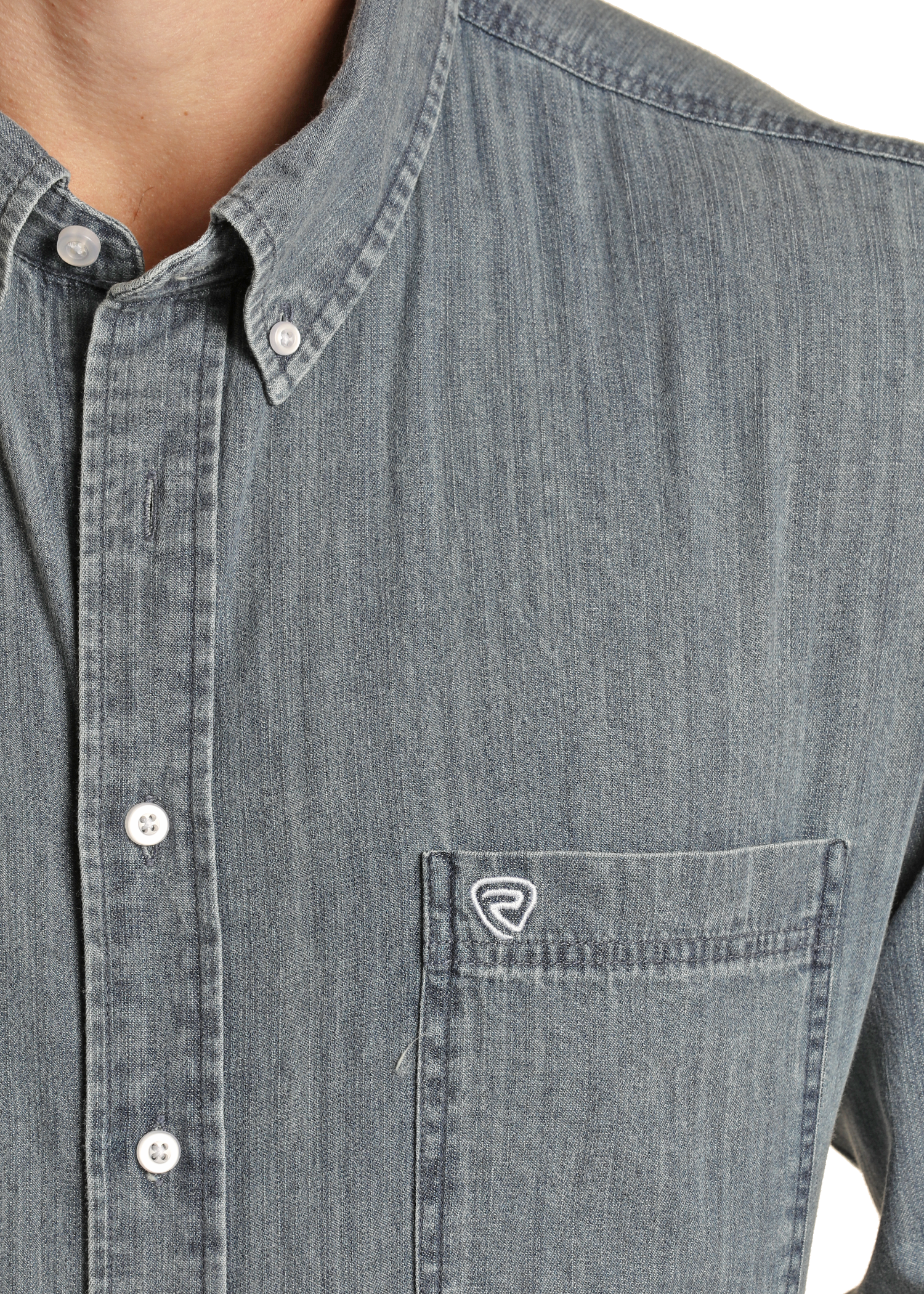 A close-up of a person wearing the Rock & Roll Denim Long Sleeve Button Shirt, featuring a chest pocket with a small white embroidered logo, button-down collar, and white buttons.