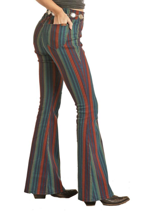 A person wearing Rock & Roll Denim Mid Rise Striped Pull-On Jeans with a colorful vertical stripe pattern and black shoes adds Western flair, shown from the side against a white background.