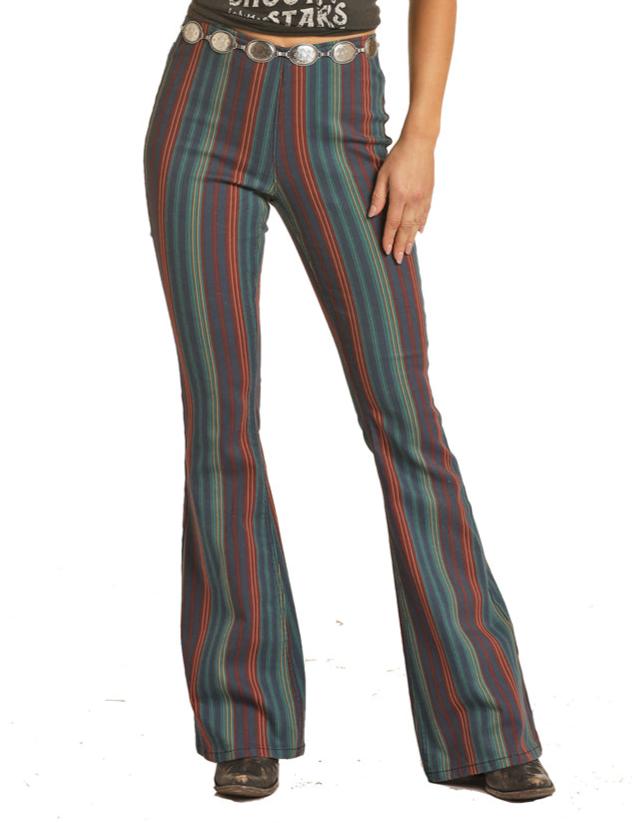 A person wears Rock & Roll Denim Mid Rise Striped Pull-On Jeans with vertical red, green, and blue stripes, paired with a black belt featuring round silver conchos and black shoes. Only the lower body is visible.