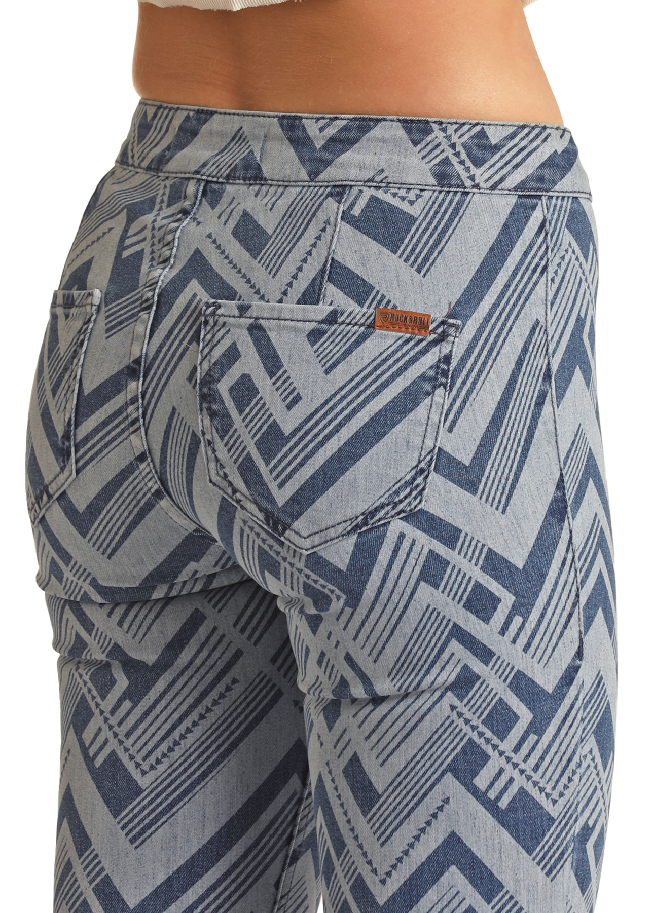 A close-up of a person wearing Rock & Roll Denim's Abstract Pattern High Rise Bell Bottom Jeans, featuring bold geometric zigzags, with the back pockets, waistband, and part of a white top visible.