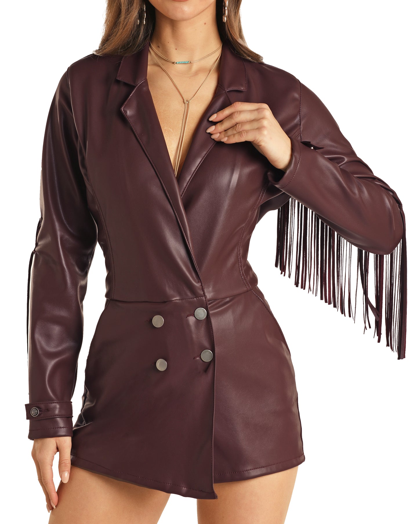 A woman models the Rock & Roll Denim Fringe Pleather Romper in burgundy, featuring fringe on one sleeve, double-breasted buttons, and a deep neckline. She rests her hand on her chest with her face partially out of frame.