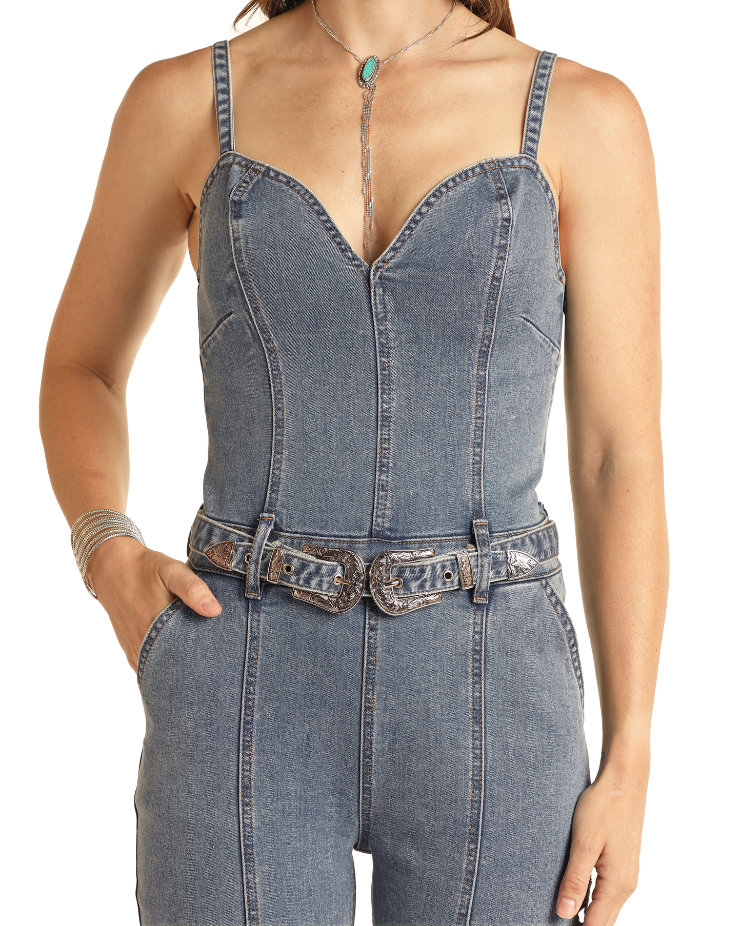 A person wears the Rock & Roll Denim Front Seams Denim Jumpsuit—sleeveless, form-fitting, medium wash with a sweetheart neckline and double buckled belt—paired with a turquoise necklace and bracelet.