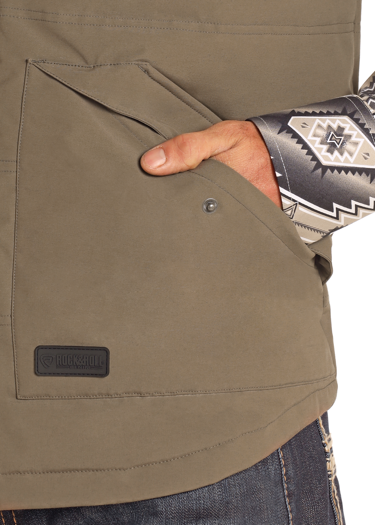 A person with a patterned sleeve slips their hand into the pocket of the Rock & Roll Denim Vintage '46 Puffer Vest in olive-green, styled above dark blue jeans for a subtle vintage look.