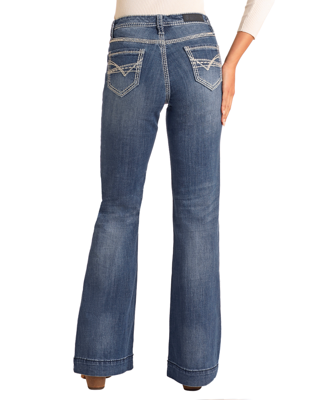 A person in Rock & Roll Denim's Mid Rise Petal Stitch Trousers, cotton denim jeans with white petal stitch embroidery on the decorative back pockets, stands facing away from the camera.