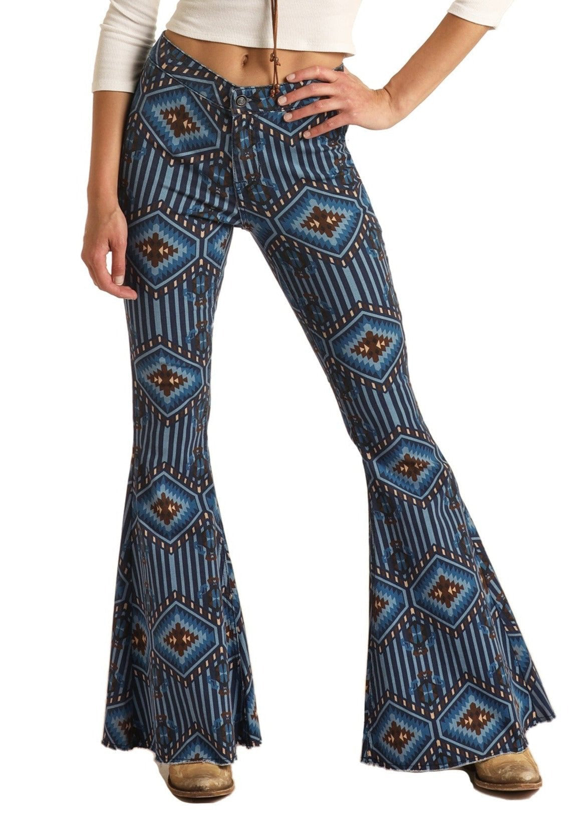 Wearing Rock & Roll Denim's Diamond Aztec High Rise Bell Bottom Jeans (26x34) with a blue geometric pattern and a white long-sleeve crop top, only the lower torso and legs are shown, emphasizing the bold southwestern style.