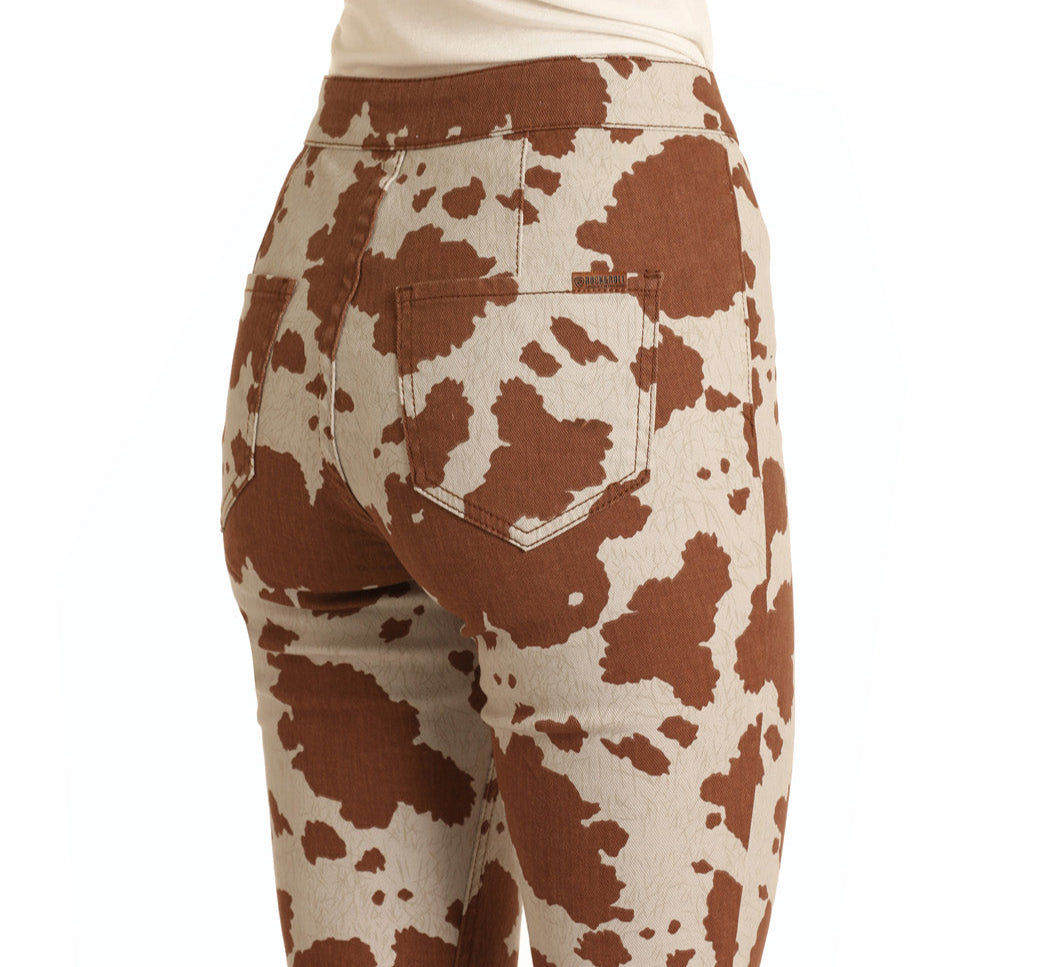 A person is shown from the back wearing Rock & Roll Denim’s Cow Print Button Bells, high-rise bell bottom jeans featuring a brown and white cow print, with focus on the hip and pocket area.