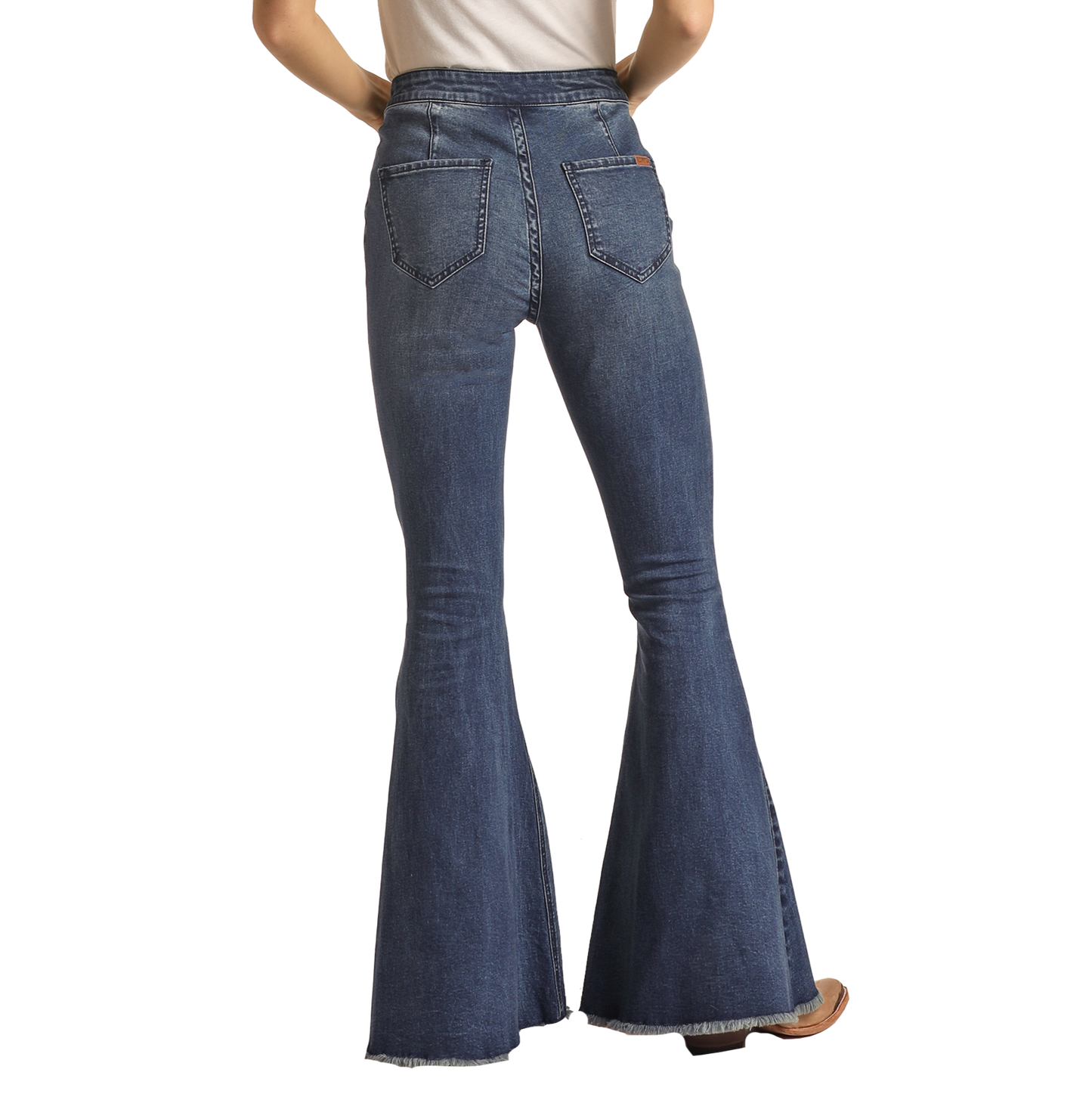 A person seen from the back wears Rock & Roll Denim’s Dark Wash High Rise Bell Bottoms with frayed hems, large back pockets, and visible stitching. The look is finished with brown shoes and a white top.