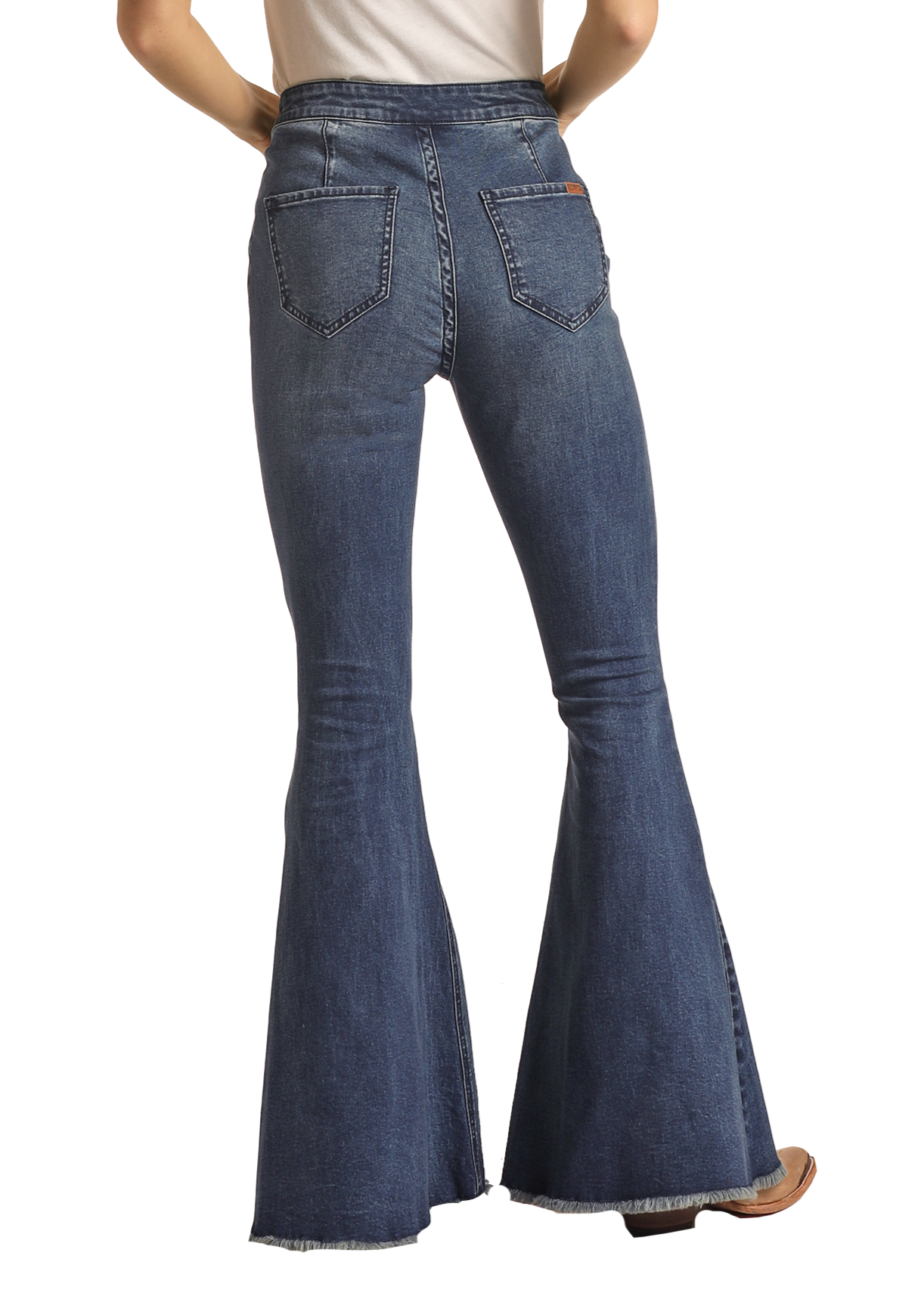 A person seen from the back wears Rock & Roll Denim’s Dark Wash High Rise Bell Bottoms with frayed hems, large back pockets, and visible stitching. The look is finished with brown shoes and a white top.