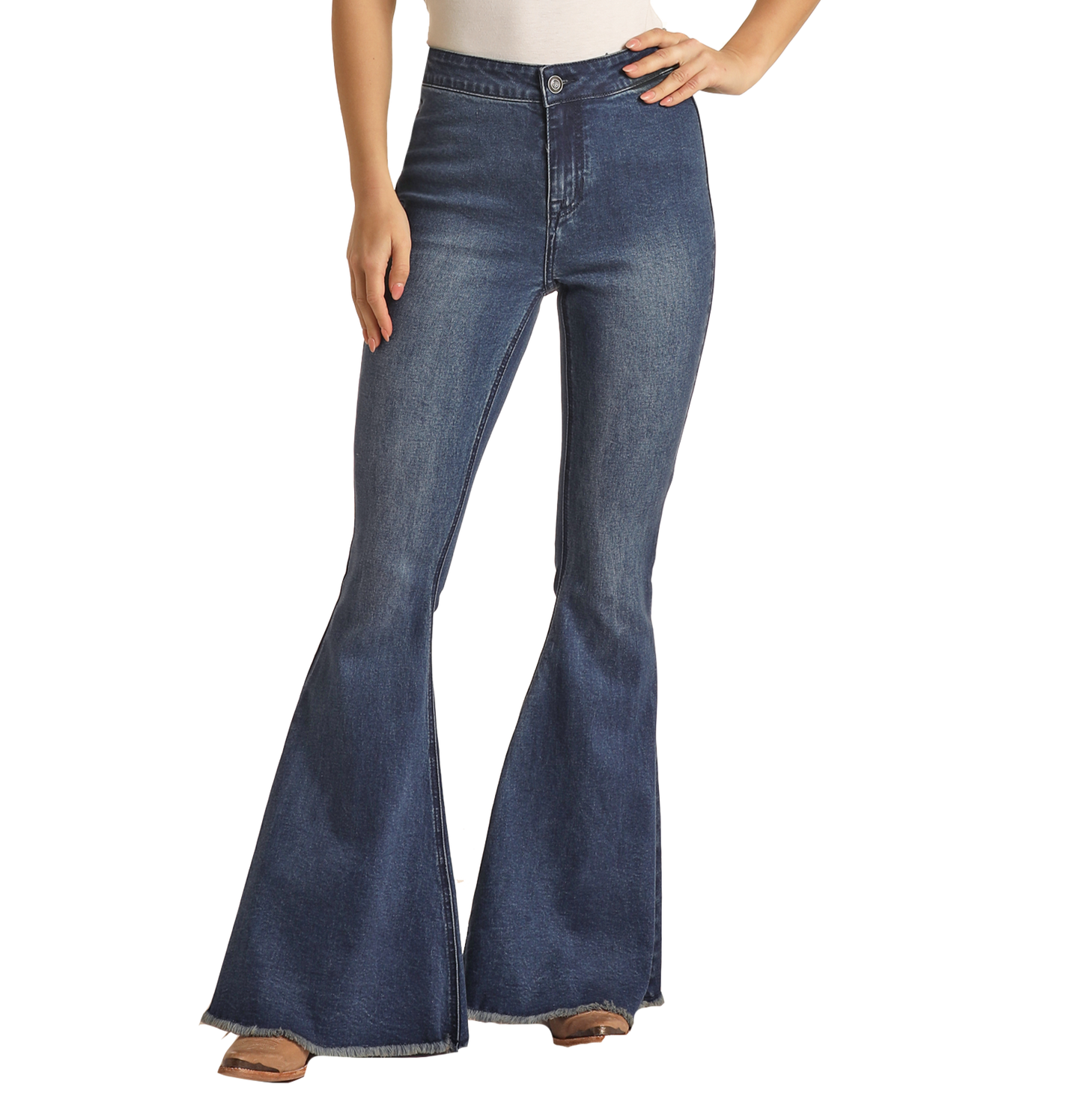 A woman stands confidently with one hand on her hip against a white background, wearing Rock & Roll Denim's Dark Wash High Rise Bell Bottoms featuring stretch denim and a raw hem, paired with tan shoes.