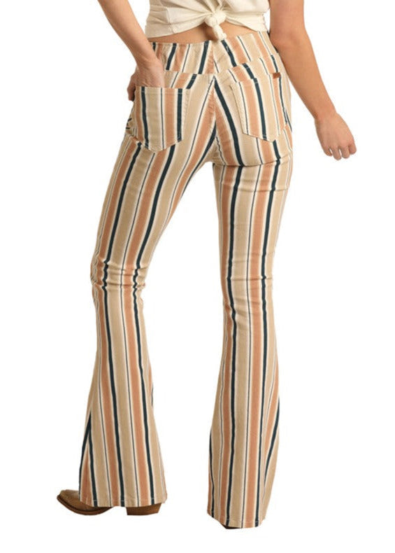 A person stands facing away, wearing Rock & Roll Denim Striped High Rise Flare Leg Jeans in beige, white, and dark blue tones, paired with a knot-tied white cotton polyester blend top and brown shoes.