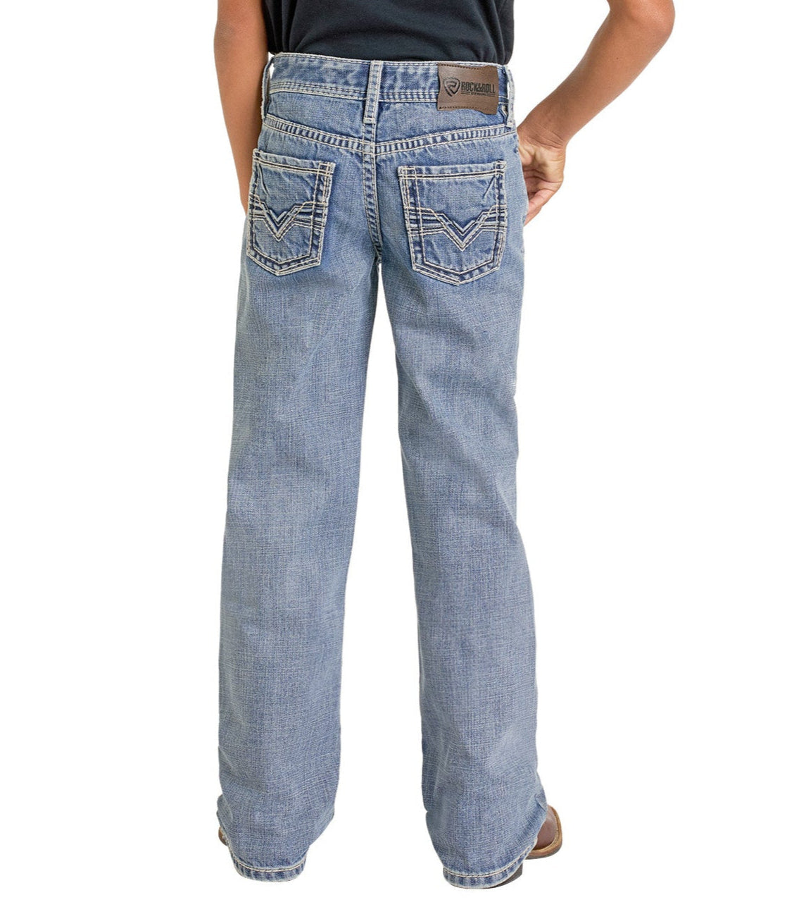 A boy is seen from behind wearing Rock & Roll Denim Boys' Regular Fit Raised Signature Bootcut Jeans in light blue, featuring decorative back pocket stitching and a brown leather brand patch.