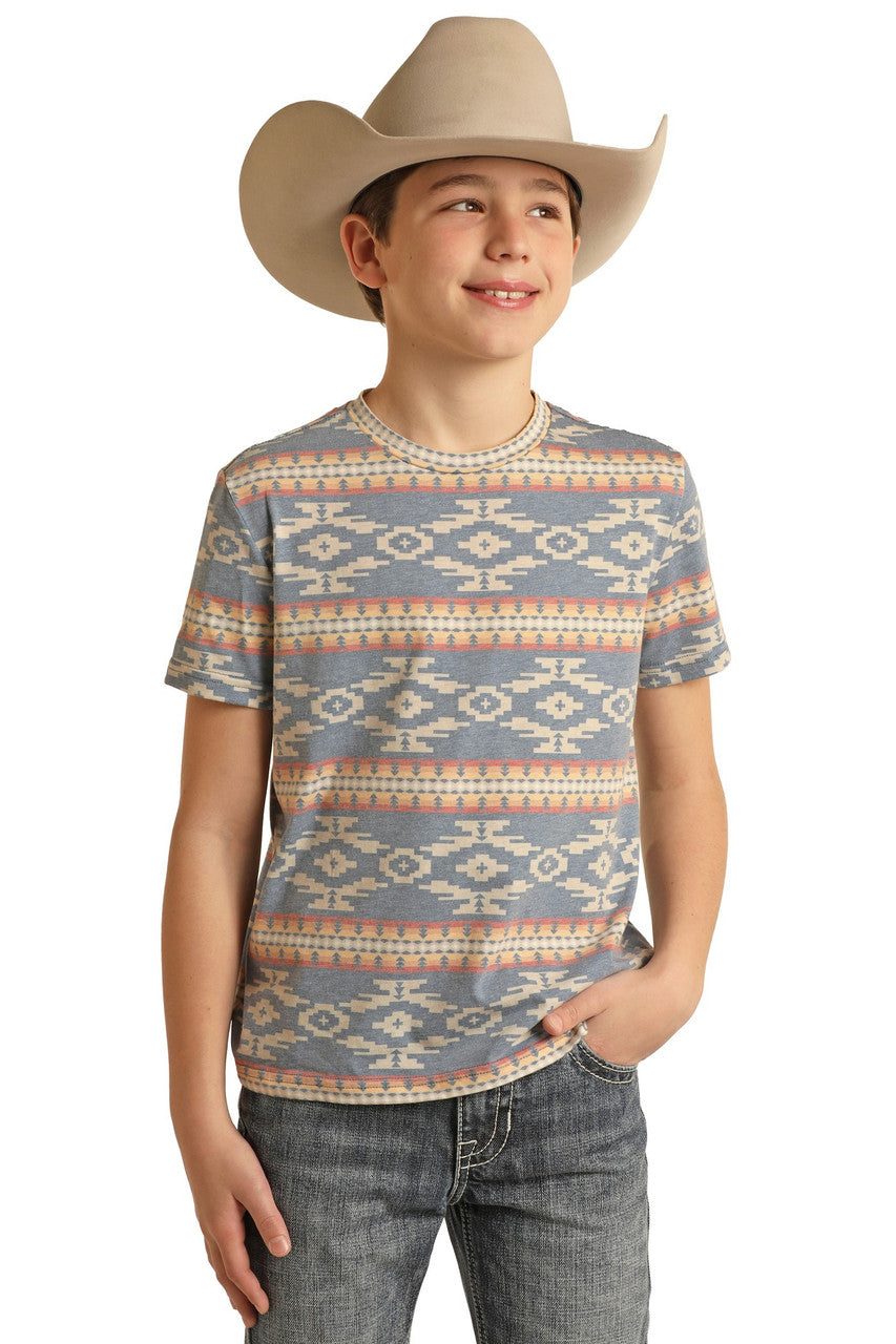 A smiling boy in a cowboy hat, Rock & Roll Denim Boys' Aztec Print T-Shirt, and jeans stands with one hand in his pocket against a white background.
